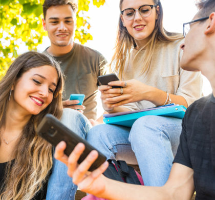 Teen group of friends with smartphones at park. Millennials best friends using mobile phones, addicted to technology and social media. Lifestyle and friendship concepts