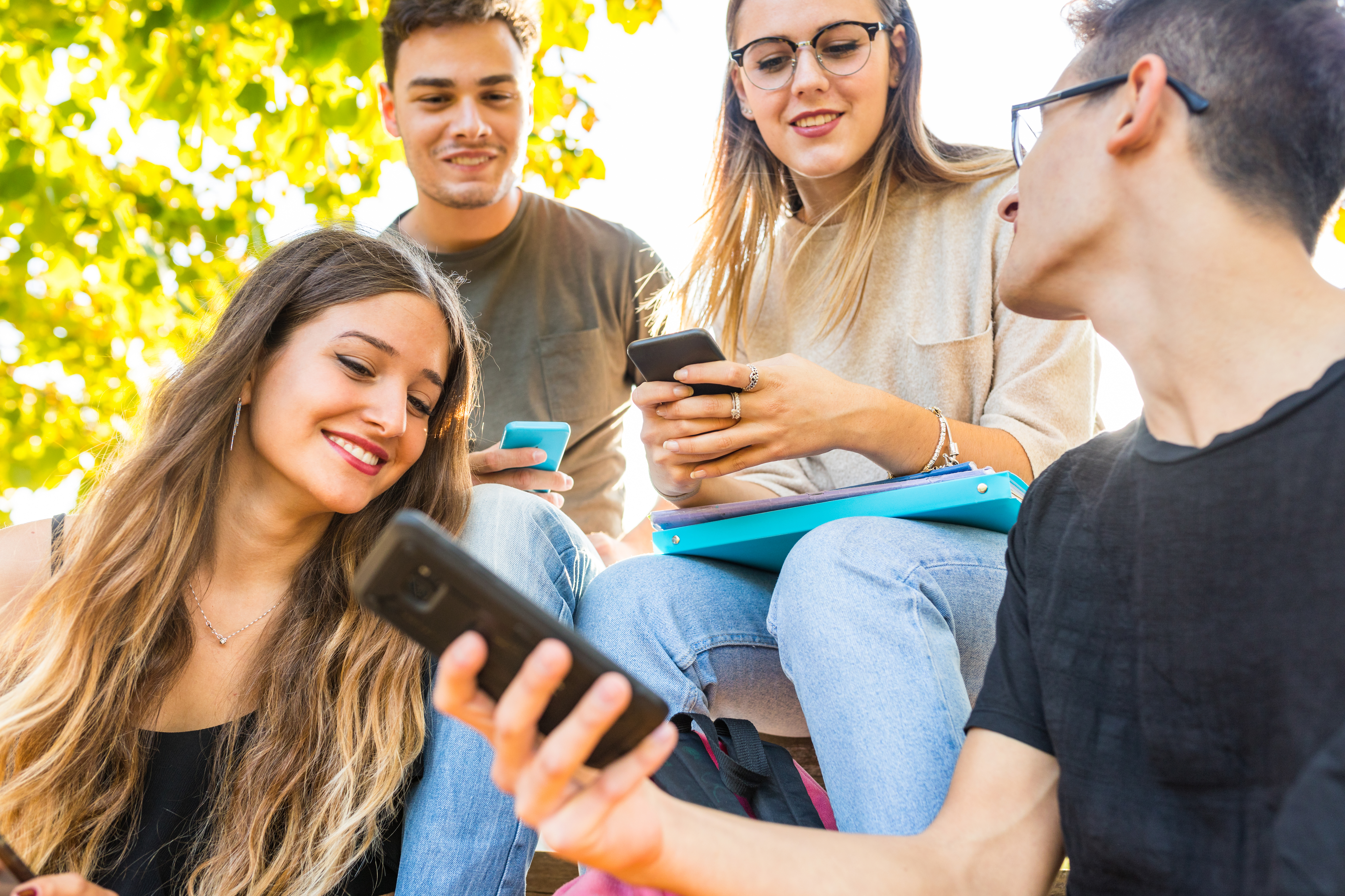 Teen group of friends with smartphones at park. Millennials best friends using mobile phones, addicted to technology and social media. Lifestyle and friendship concepts